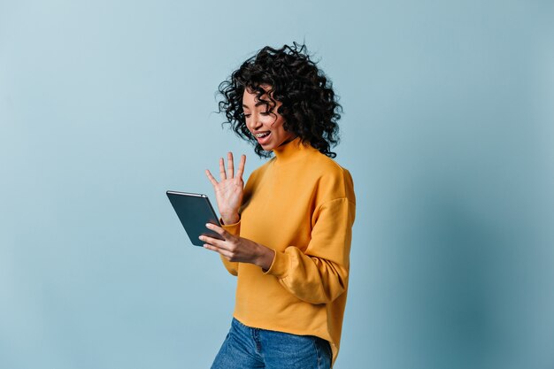 Mujer sonriente agitando la mano en la pantalla de la tableta digital