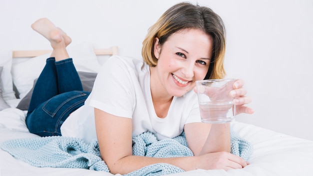 Mujer sonriente con agua acostada en la cama