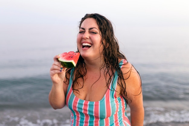 Mujer sonriente en el agua en la playa comiendo sandía