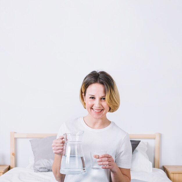 Mujer sonriente con agua posando en la cama