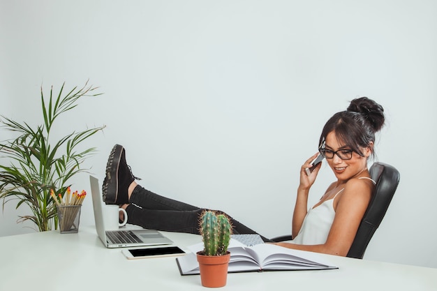 Mujer sonriente al teléfono y con los pies sobre el escritorio