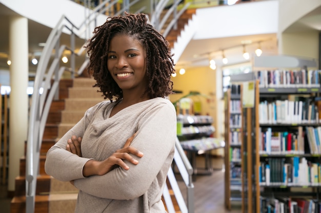 Foto gratuita mujer sonriente alegre que presenta en la biblioteca pública