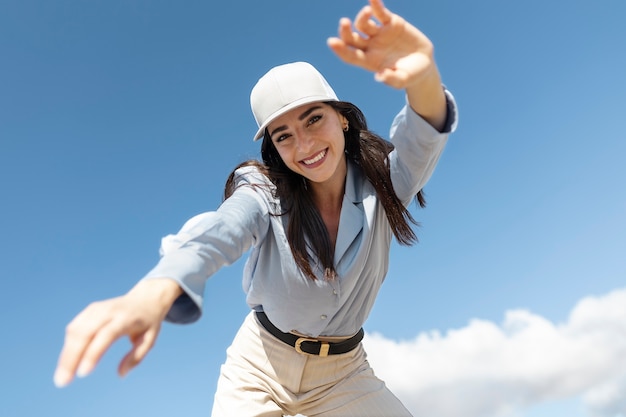 Mujer sonriente de ángulo bajo posando con sombrero de camionero