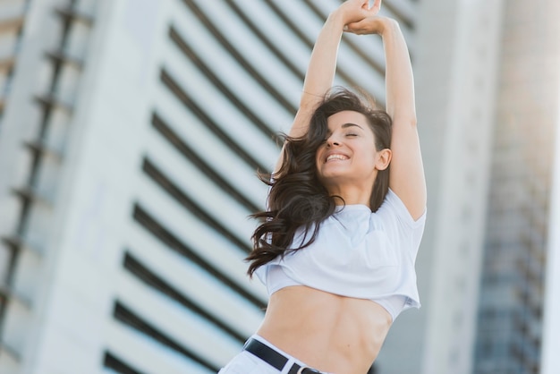 Mujer sonriente de ángulo bajo en ropa blanca posando