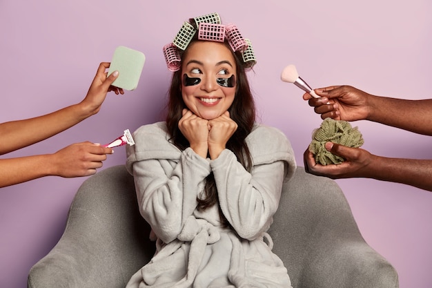 Mujer sonriente aplica parches en los ojos y rizadores para el cabello, rodeada de muchas esteticistas