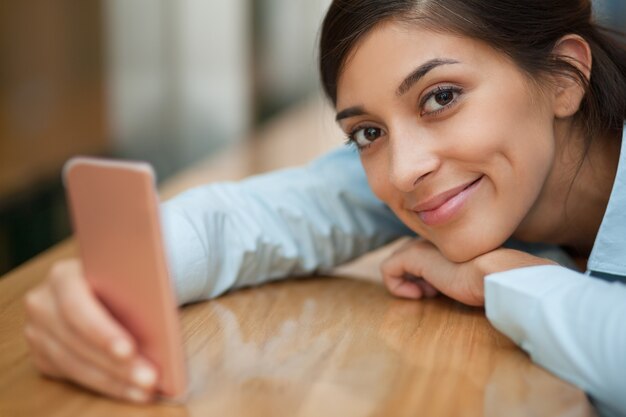 Mujer sonriente apoyándose en la mesa con Smartphone