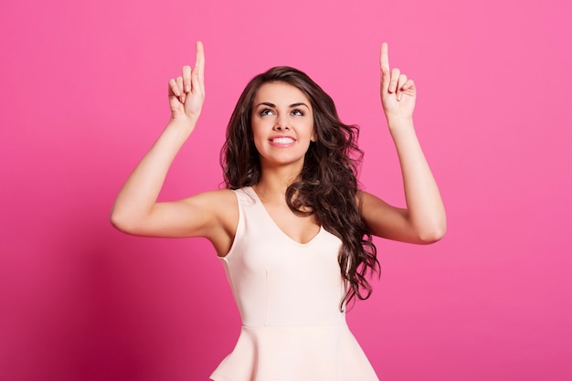 Mujer sonriente apuntando hacia arriba en el espacio de copia rosa