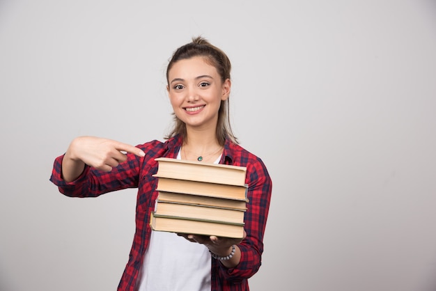 Foto gratuita una mujer sonriente apuntando a una pila de libros.