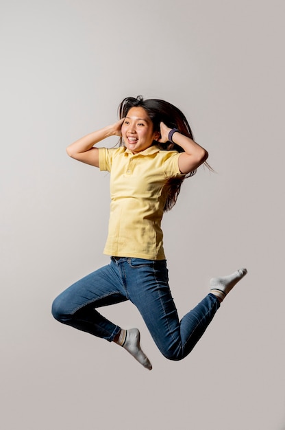 Mujer sonriente asiática que salta en estudio