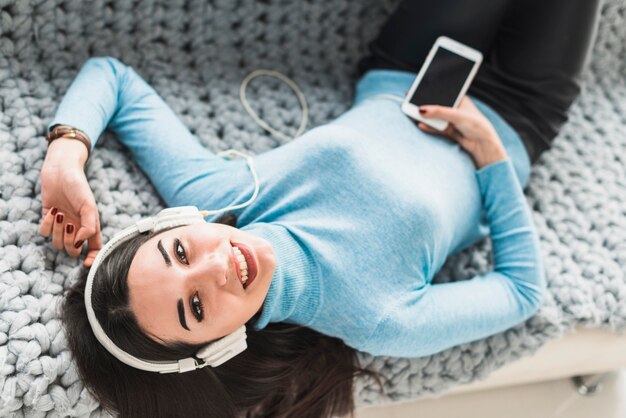 Mujer sonriente en auriculares acostado en el sofá