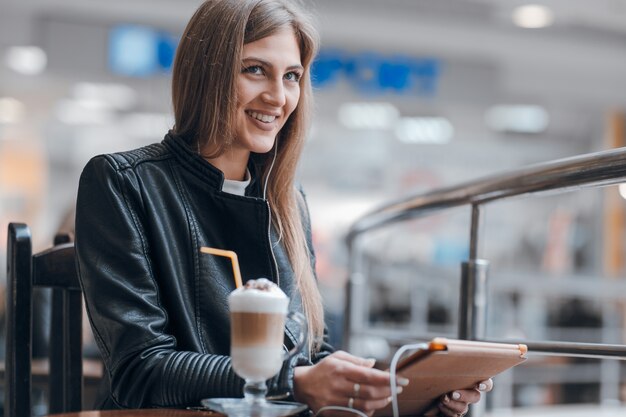 Mujer sonriente con auriculares blancos y un batido en la mesa