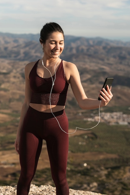 Mujer sonriente con auriculares mirando móvil