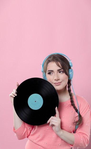 Mujer sonriente con auriculares posando con disco de vinilo