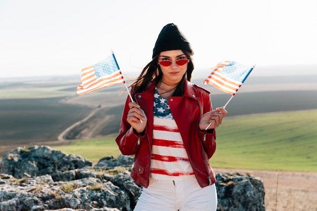 Mujer sonriente con banderas americanas posando en la cima de la montaña