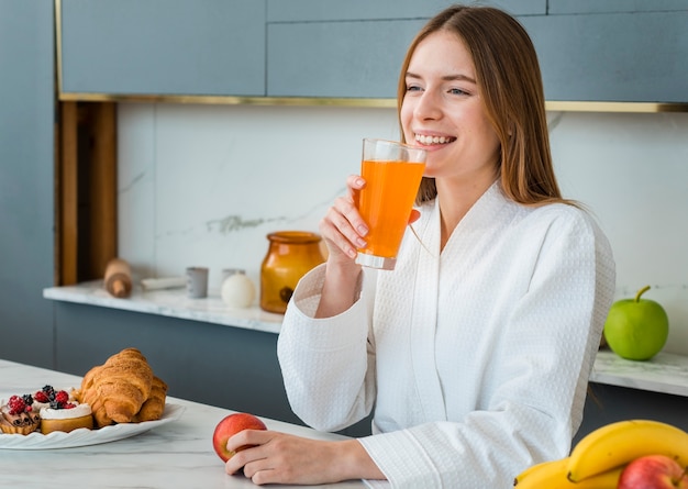 Mujer sonriente en bata de baño beber jugo