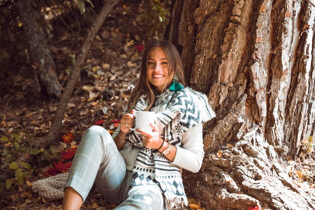 Mujer sonriente con bebida en el bosque