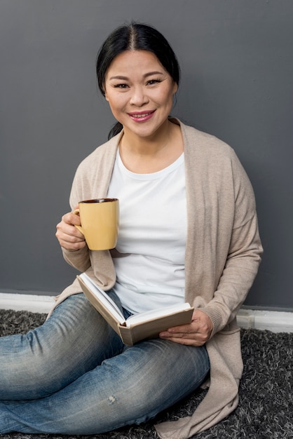 Mujer sonriente bebiendo café y leyendo