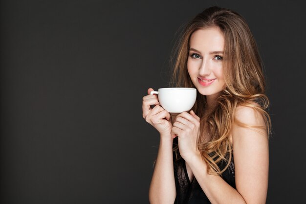 Mujer sonriente bebiendo café sobre pared oscura