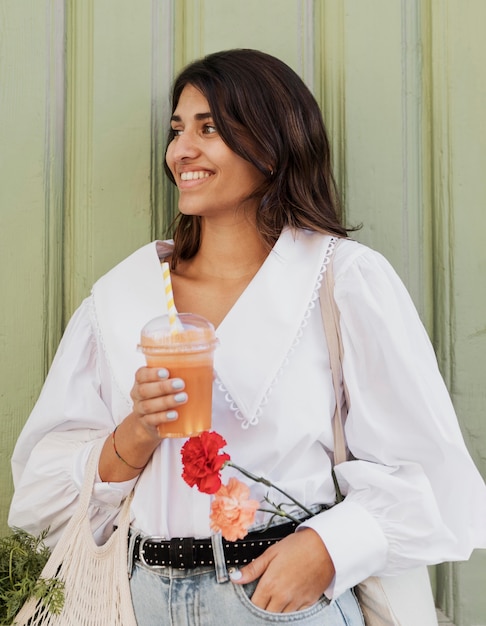 Mujer sonriente con bolsas de la compra y flores con jugo al aire libre