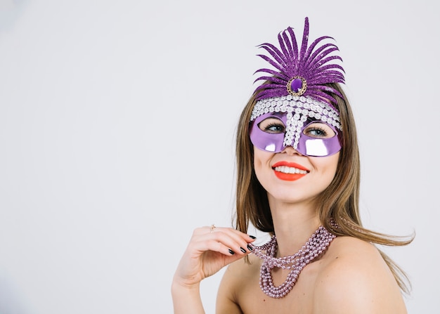 Mujer sonriente bonita que lleva la máscara decorativa púrpura del carnaval en el fondo blanco