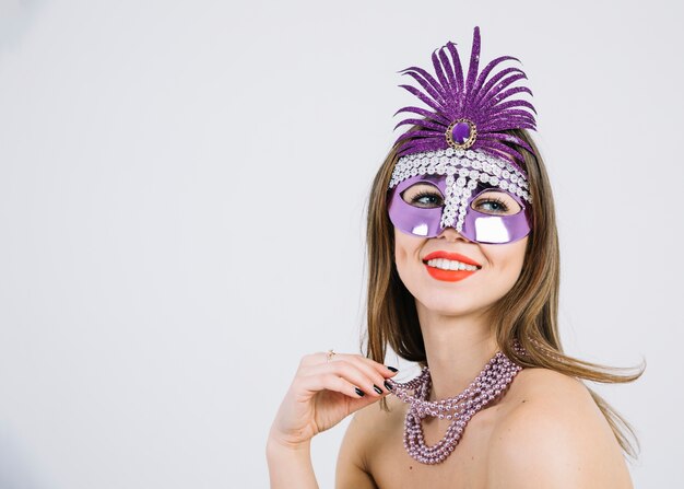 Mujer sonriente bonita que lleva la máscara decorativa púrpura del carnaval en el fondo blanco