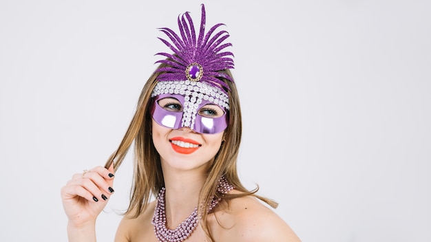 Mujer sonriente bonita que lleva la máscara decorativa púrpura del carnaval en el fondo blanco