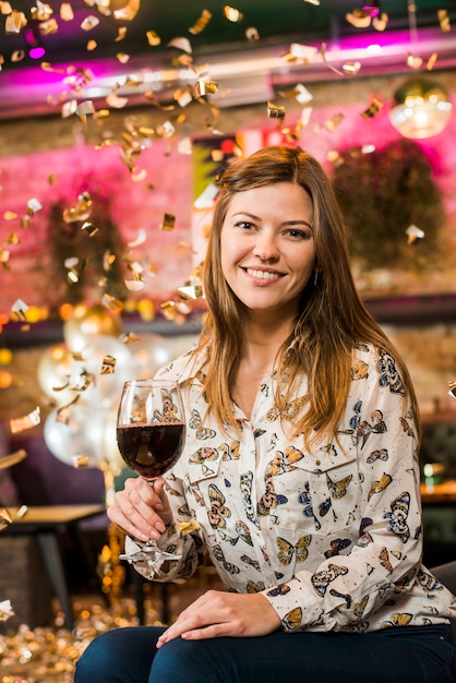 Mujer sonriente bonita que sostiene el vidrio de vino que disfruta del partido