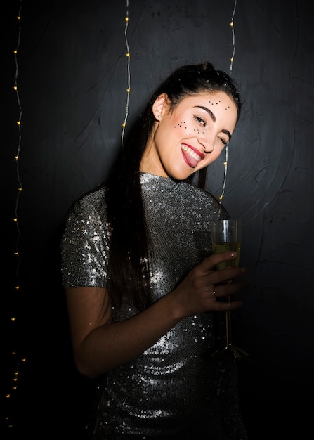 Mujer sonriente con brillos en cara sosteniendo vaso de bebida