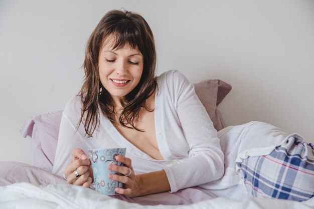 Mujer sonriente con café tumbada en la cama