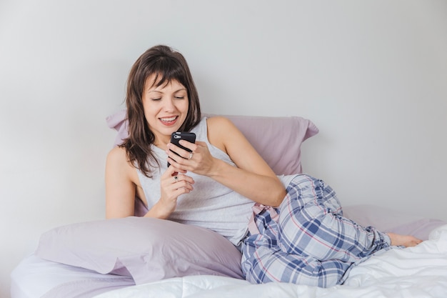 Mujer sonriente en cama escribiendo en smartphone