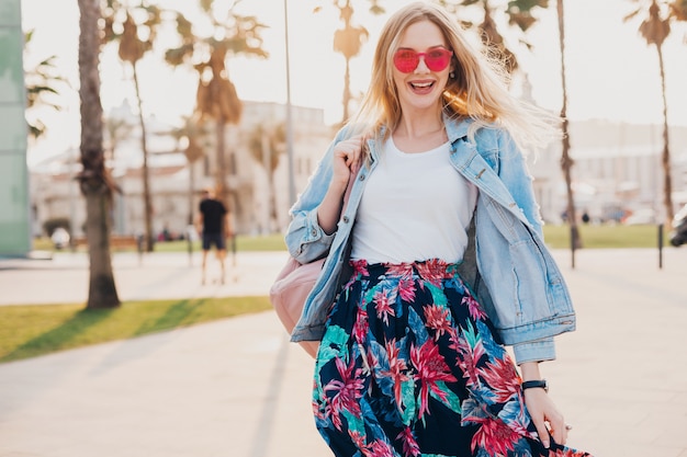 Foto gratuita mujer sonriente caminando en las calles de la ciudad con elegante falda estampada y chaqueta vaquera de gran tamaño con gafas de sol rosa