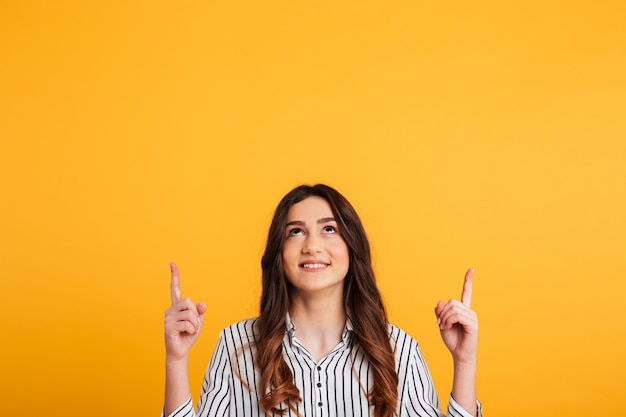 Mujer sonriente en camisa apuntando y mirando hacia arriba