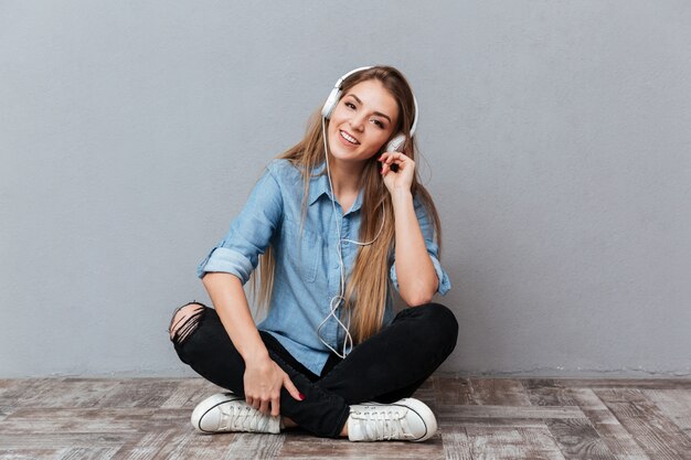 Mujer sonriente en camisa escuchando música en el piso