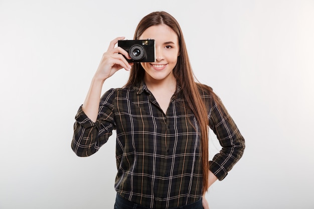 Mujer sonriente en camisa haciendo fotos en cámara retro