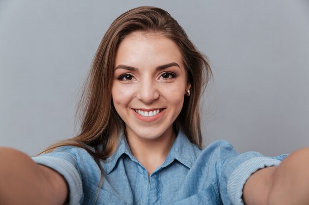 Mujer sonriente en camisa haciendo selfie en estudio