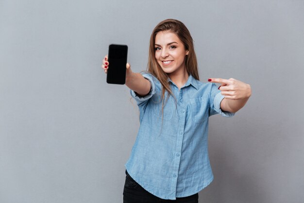 Mujer sonriente en camisa mostrando la pantalla del teléfono inteligente en blanco