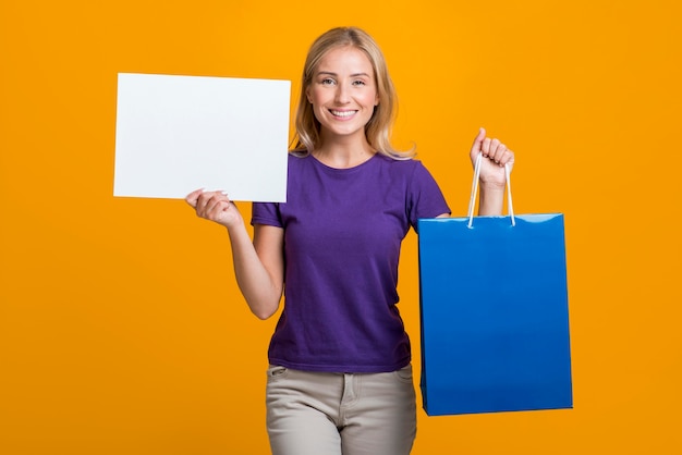 Mujer sonriente con cartel en blanco y bolsa de compras