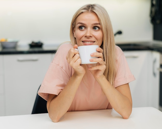 Mujer sonriente en casa durante la pandemia tomando una taza de café