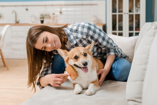 Mujer sonriente cepillando a su perro en el sofá