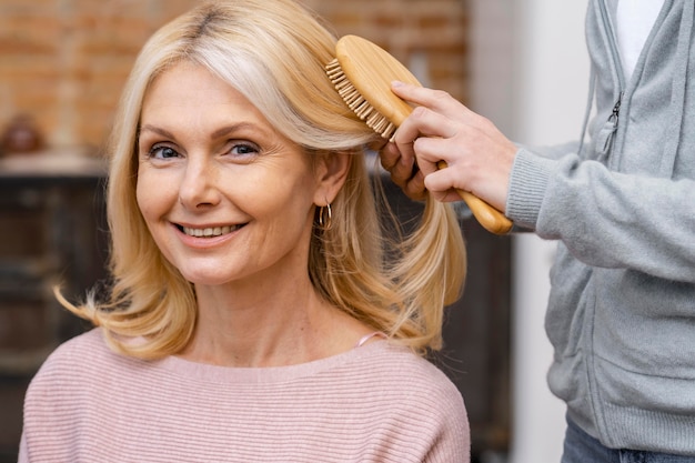 Foto gratuita mujer sonriente a cepillarse el cabello en el salón por esteticista