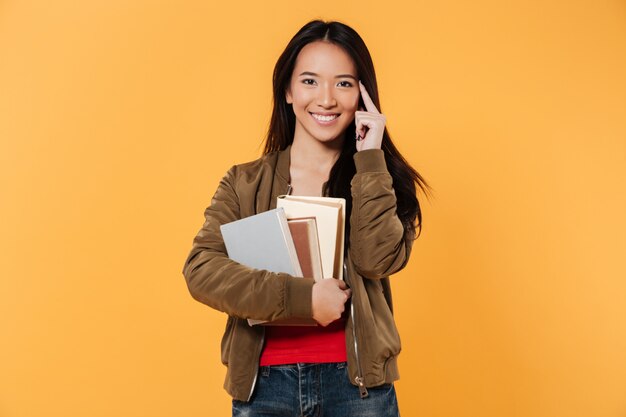 Mujer sonriente en chaqueta sosteniendo libros mientras mira a la cámara