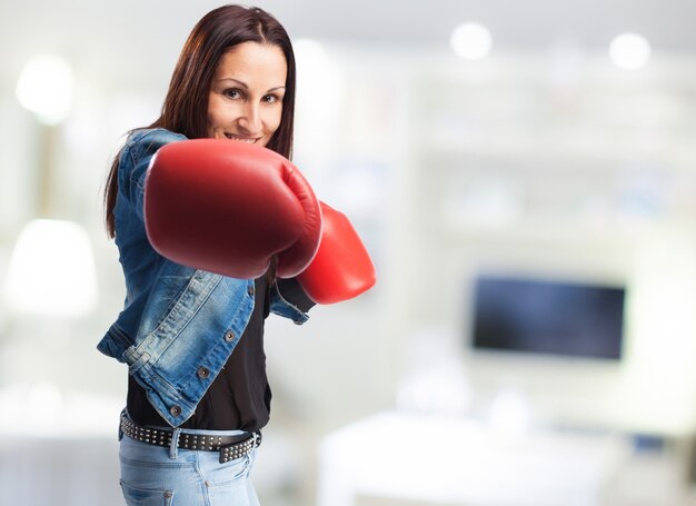 Mujer sonriente en chaqueta vaquera con guantes de boxeo dando un puñetazo