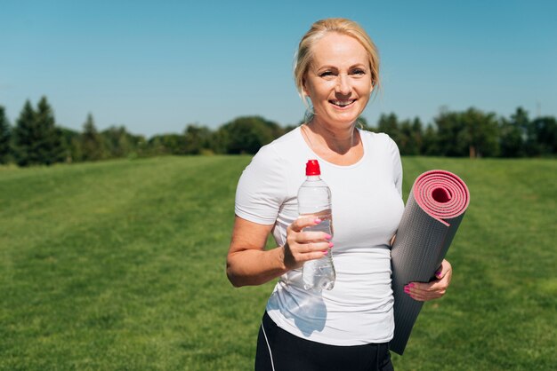 Mujer sonriente con colchoneta de yoga y botella de agua