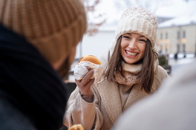 Mujer sonriente comiendo una hamburguesa con sus amigos después de una larga reunión