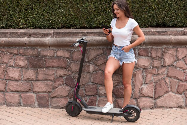 Mujer sonriente comprobando su teléfono inteligente mientras está en scooter eléctrico