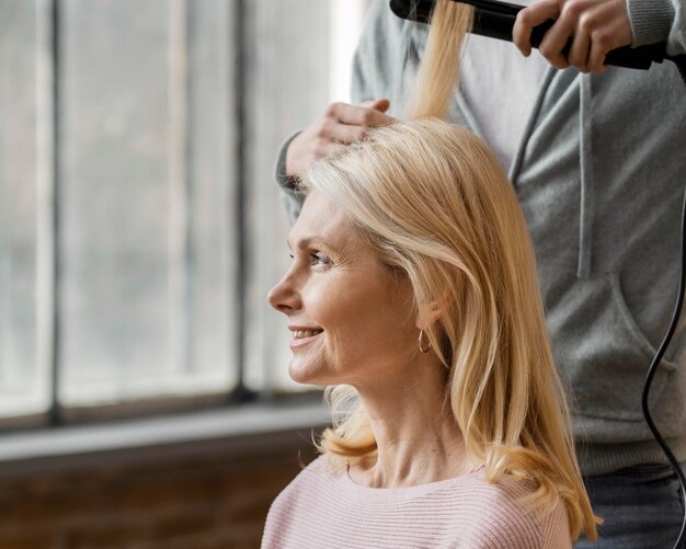 Mujer sonriente conseguir su cabello alisado por peluquero en casa