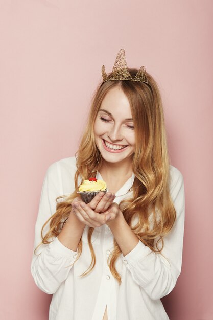 Mujer sonriente, con una corona, sosteniendo un cupcake de cumpleaños