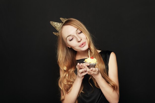 Mujer sonriente, con una corona, sosteniendo un cupcake de cumpleaños