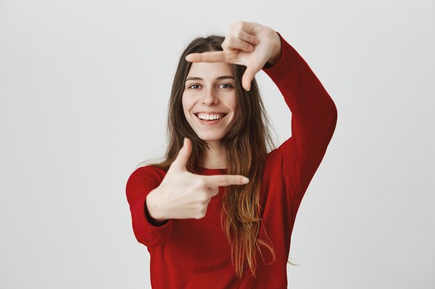 Mujer sonriente creativa buscando inspiración, hacer gestos de marcos de cámara