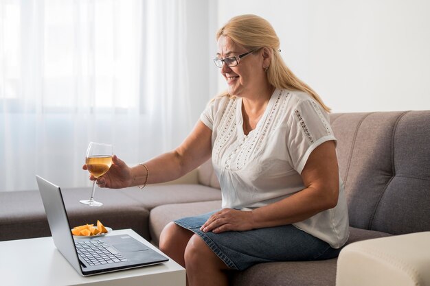 Mujer sonriente en cuarentena tomando una copa con el portátil